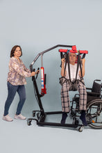 hombre elevado con una grúa para pacientes, manejada por su cuidadora