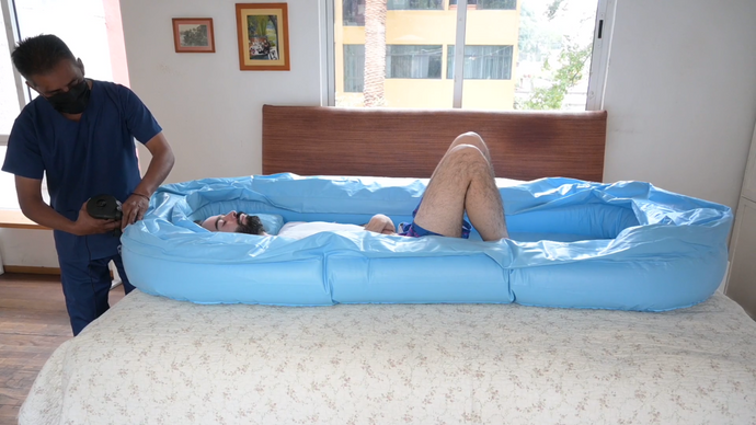 Imagen de un cuidador inflando una bañera portátil colocada sobre una cama con un paciente dentro de ella