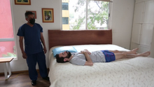 Paciente en cama mientras un cuidador prepara una bañera portátil